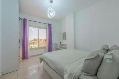 a bedroom with a bed with purple curtains and a window at Luxury apartment on the pool in Hurghada