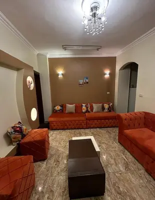 a living room with orange couches and a chandelier at Luxe Nest Luxor Serviced Apartments 101 in Luxor