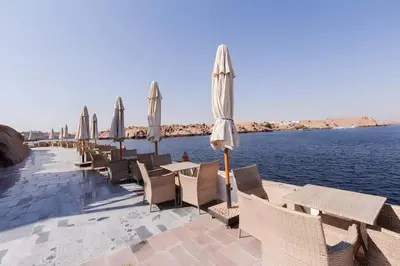 a row of tables and chairs with umbrellas and water at Aro Kato Nubian Guest House in Aswan