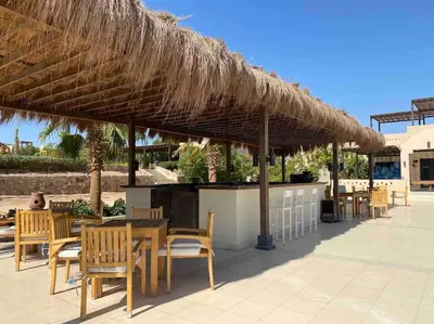 a restaurant with tables and chairs under a straw umbrella at Relaxing time in Makadi Heights in Hurghada