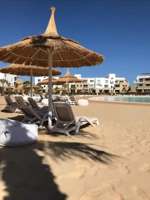 a group of chairs and an umbrella on a beach at Modern chalet at el gouna Swan Lake compound with Swimable lagoon view in Hurghada