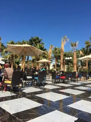 a patio with chairs and tables and umbrellas and palm trees at ميراج باي in Hurghada