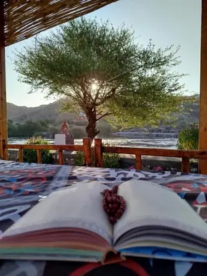 an open book on a bed with a tree in the background at ASSINGAR camp in Jazīrat Suhayl