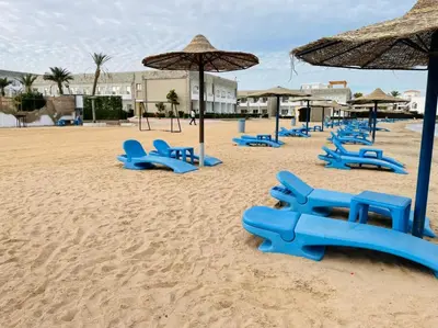 a sandy beach with blue chairs and umbrellas at Cecilia resort hurghadaمنتجع سيسيليا in Hurghada