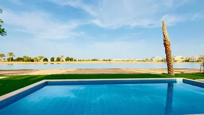 a swimming pool with a palm tree and a body of water at Ollystays 4BR Villa Heated Pool El Gouna in Hurghada