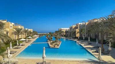 a large swimming pool with palm trees and buildings at Ollystays Mangroovy Seaview 2BR Beach and Pool Free access in Hurghada