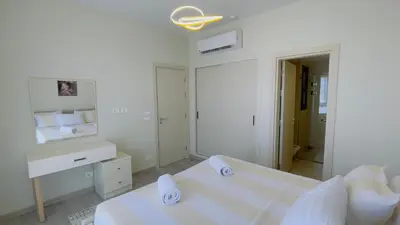 a white bedroom with a bed and a mirror at Ollystays Shedwan 1BR Pool & lagoon access in Hurghada