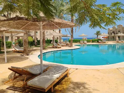 a swimming pool with chairs and an umbrella at Cozy Sunny Studio with Pool View - Sahl Hasheesh in Hurghada