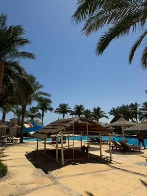 a resort with a pool and a straw umbrella and palm trees at Cozy Sunny Studio with Pool View - Sahl Hasheesh in Hurghada