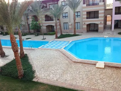 a swimming pool in front of a building with palm trees at Cozy studio with a view in port ghalib in Marsa Alam