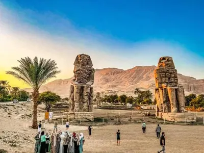 a group of people standing in front of two stone statues at البعيرات in Al Karnak