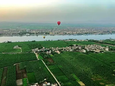 two hot air balloons are flying over a river at Luxor in Luxor
