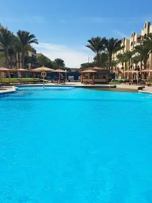 a large blue swimming pool with palm trees and buildings at Beach front 2BR at elkarma hotel & aqua park in Hurghada