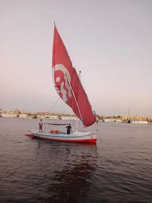 a boat with a red sail on the water at Alex in Luxor