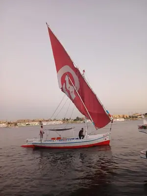 a boat with a red sail on the water at Alex in Luxor