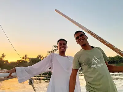 two men are standing on a boat in the water at Alex in Luxor