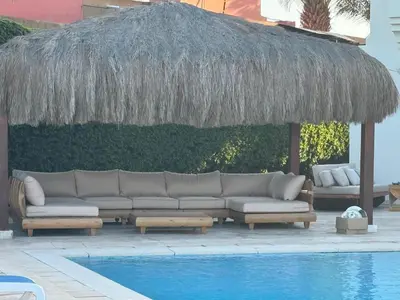 a couch under a straw umbrella next to a swimming pool at Luxury villa west golf in Hurghada