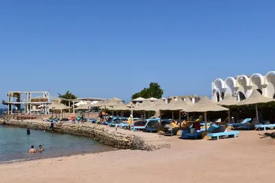 a beach with umbrellas and people in the water at New Geisum Resort in Hurghada