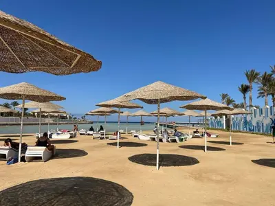 a beach with many straw umbrellas and people sitting at Scandic resort hurghada in Hurghada