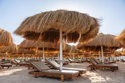 a bunch of chairs and straw umbrellas on a beach at Sunrise Solara Aqua park Resort in Banī Ghālib
