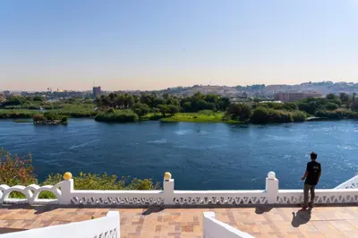 a man standing on a white fence overlooking a river at Moon of Nuba House in Aswan