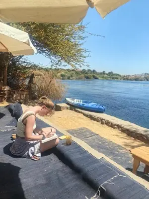 a woman sitting on the ground next to the water at Nala Narty Nubian House & Organic Farm in Aswan
