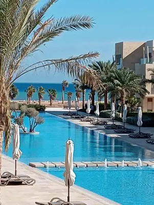 a swimming pool with chaise lounges and palm trees at Pool & Sea View 2BR in Mangroovy in Hurghada