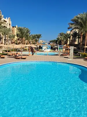 a large blue swimming pool with palm trees and buildings at Studio in elkarma resort & aqua park in Hurghada