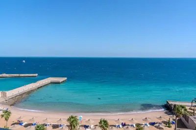 a beach with chairs and umbrellas and the ocean at Strandapartment mit Meerblick & Pool im Juliana Beach Resort, Hurghada in Hurghada