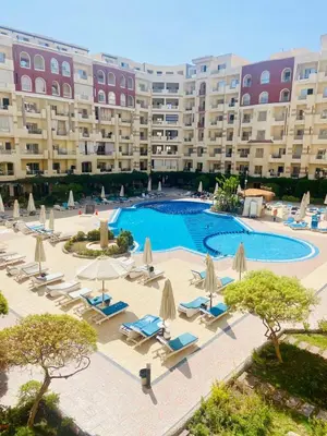 an outdoor swimming pool with lounge chairs and umbrellas at Florenza Khamsin Resort compound in Hurghada