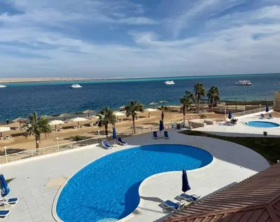 a swimming pool with chairs and the ocean in the background at Studio By The Beach in Hurghada