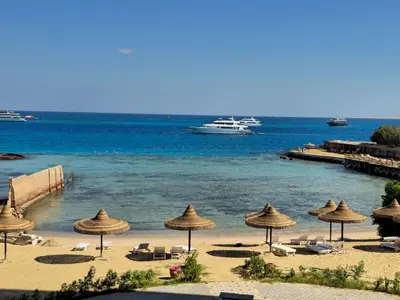 a beach with umbrellas and a boat in the water at Dive Hostel Hurghada Beach in Hurghada