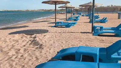 a row of blue chairs and umbrellas on a beach at Lovely APT Sunny Beach Front, Near Senzo Mall Free WIFI in Hurghada