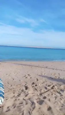 a beach with a striped umbrella on the sand at شالية بقرية الذهبية in Hurghada