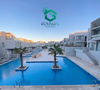 a swimming pool with palm trees in front of some buildings at Sholan, 1 Bedroom, Ground floor in Hurghada