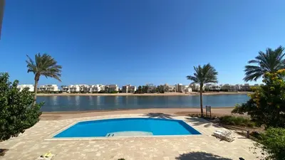 a swimming pool next to a body of water with palm trees at SunShine Joubal view in Hurghada