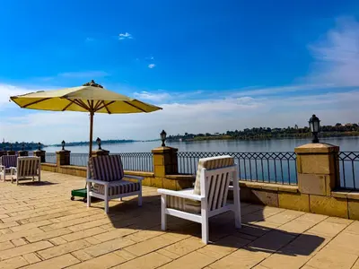 a patio with chairs and an umbrella next to the water at Stunning Nile view Apartment in Luxor