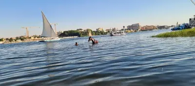 a woman standing in the water with a sail boat at Nile House Anis & Do in Luxor