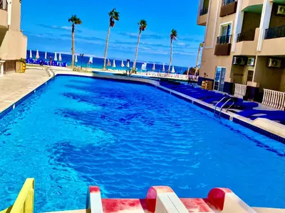 a large swimming pool next to a building with palm trees at Juliana Beach in Hurghada