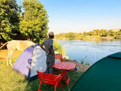 a man standing next to a tent next to a river at Anoosh camp in Aswan