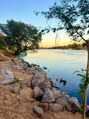 a river with rocks and a sunset in the background at Anoosh camp in Aswan