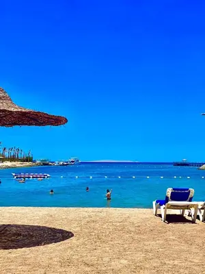 a beach with two chairs and people in the water at Mirage bay resort in Hurghada