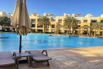 a large swimming pool with an umbrella and a table and chairs at Mangroovy 1 br Ground Composure & Cool Hilton view in Hurghada