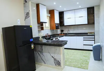 a kitchen with a black refrigerator and white cabinets at Peaceful Magawish Apartment in Hurghada