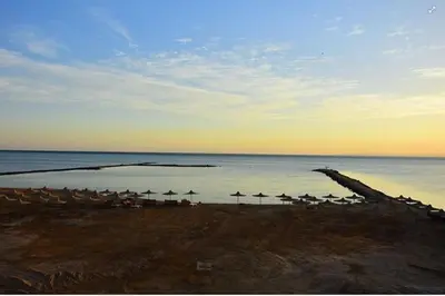 a beach with umbrellas and the ocean with the sun setting at Impeccable 1-Bed Apartment in Hurghada in Hurghada