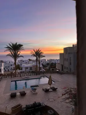 a view of a pool with palm trees and a sunset at A dream with a sea view in Azzurra in Hurghada