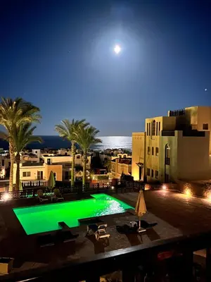 a green swimming pool with palm trees and buildings at A dream with a sea view in Azzurra in Hurghada