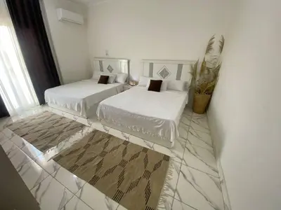 a white room with two beds and a potted plant at Asmara Apartment Hatshepsut in Naj‘ al Madāmūd