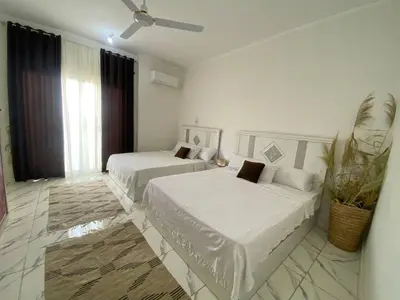 a white bedroom with two beds and a fan at Asmara Apartment Hatshepsut in Naj‘ al Madāmūd