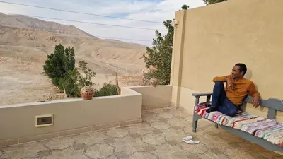 a man sitting on a bench looking out over the desert at House Mountain in Luxor